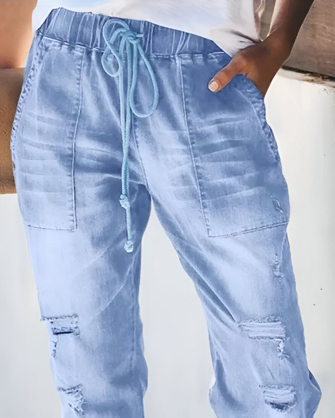 Une image d'un pantalon en jean bleu clair déchiré avec un cordon de serrage bleu à la taille.