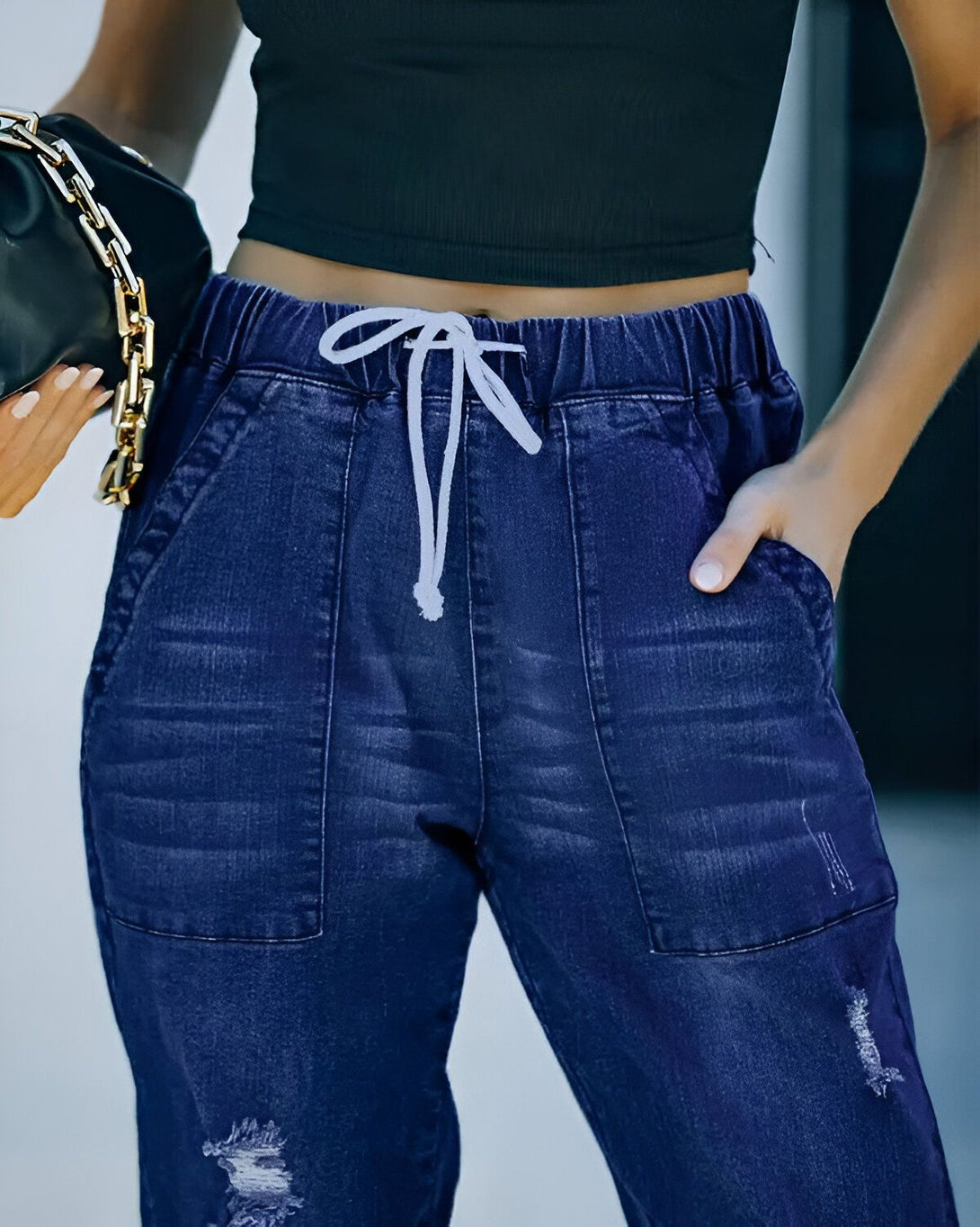 Une image d'une femme portant un jean bleu troué et déchiré, avec une poche et un cordon de serrage à la taille.