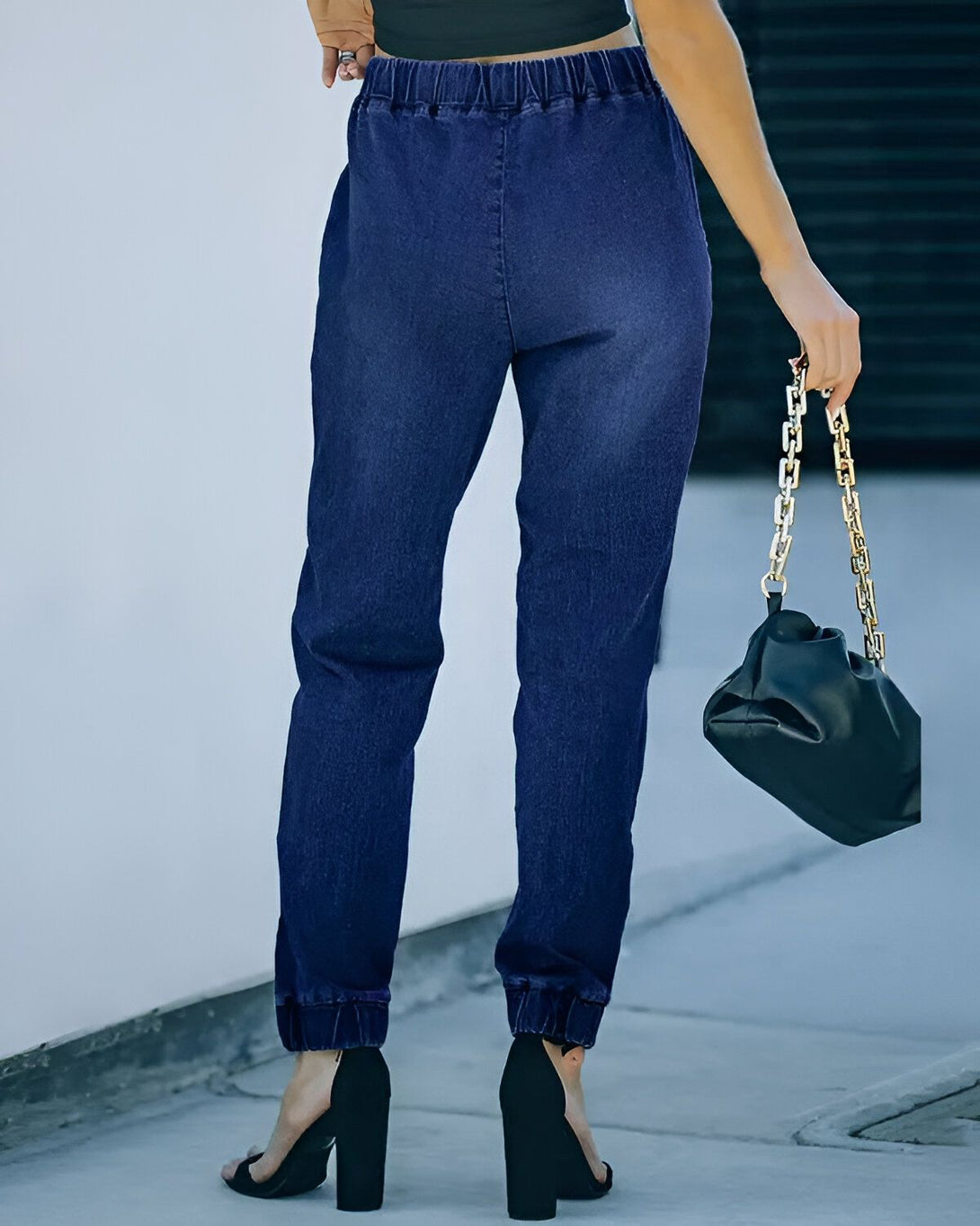 Une femme porte un jean bleu marine et un haut noir. Elle porte également des talons noirs et un sac à main noir.