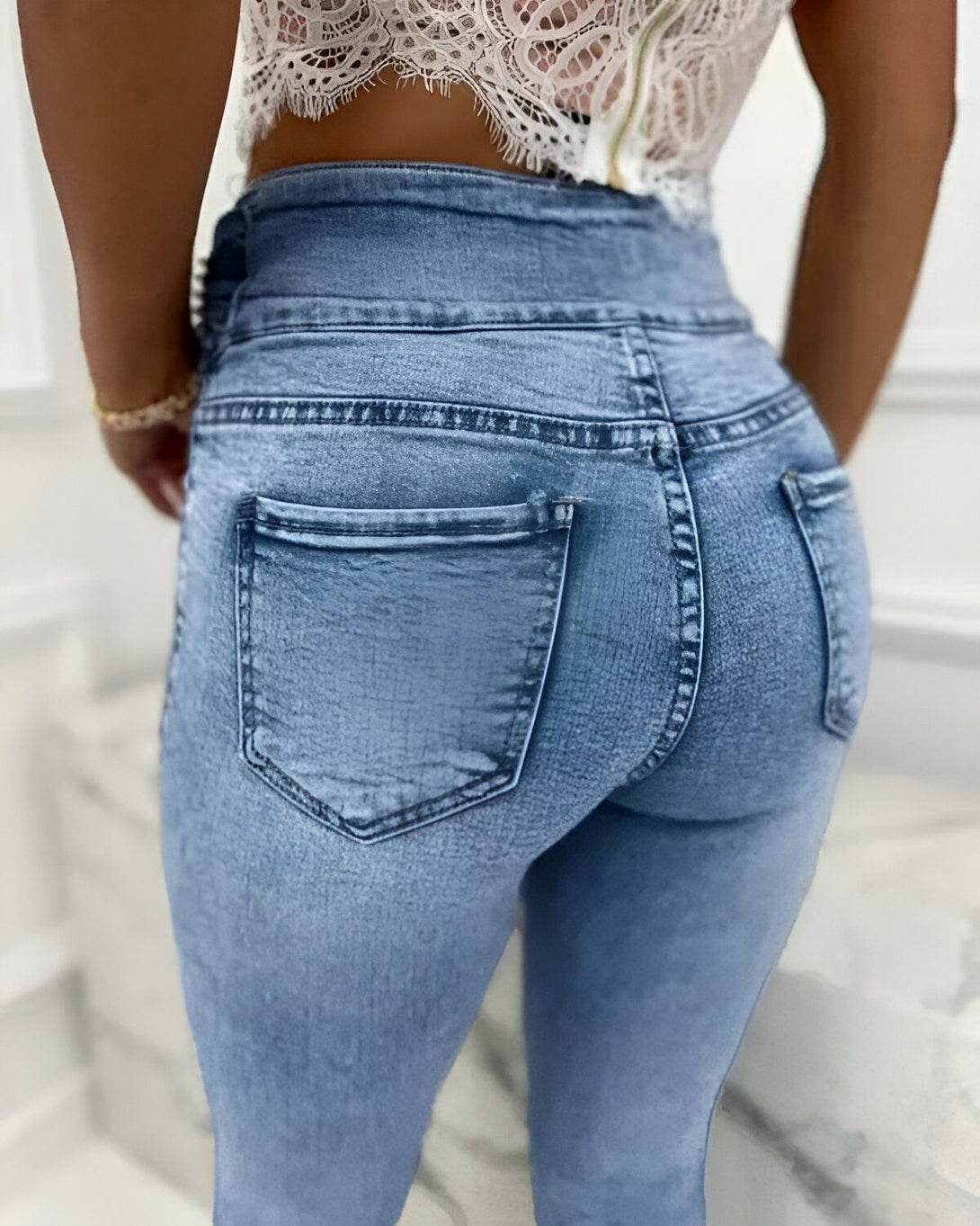 Une femme porte un jean moulant bleu clair taille haute avec une dentelle blanche.
