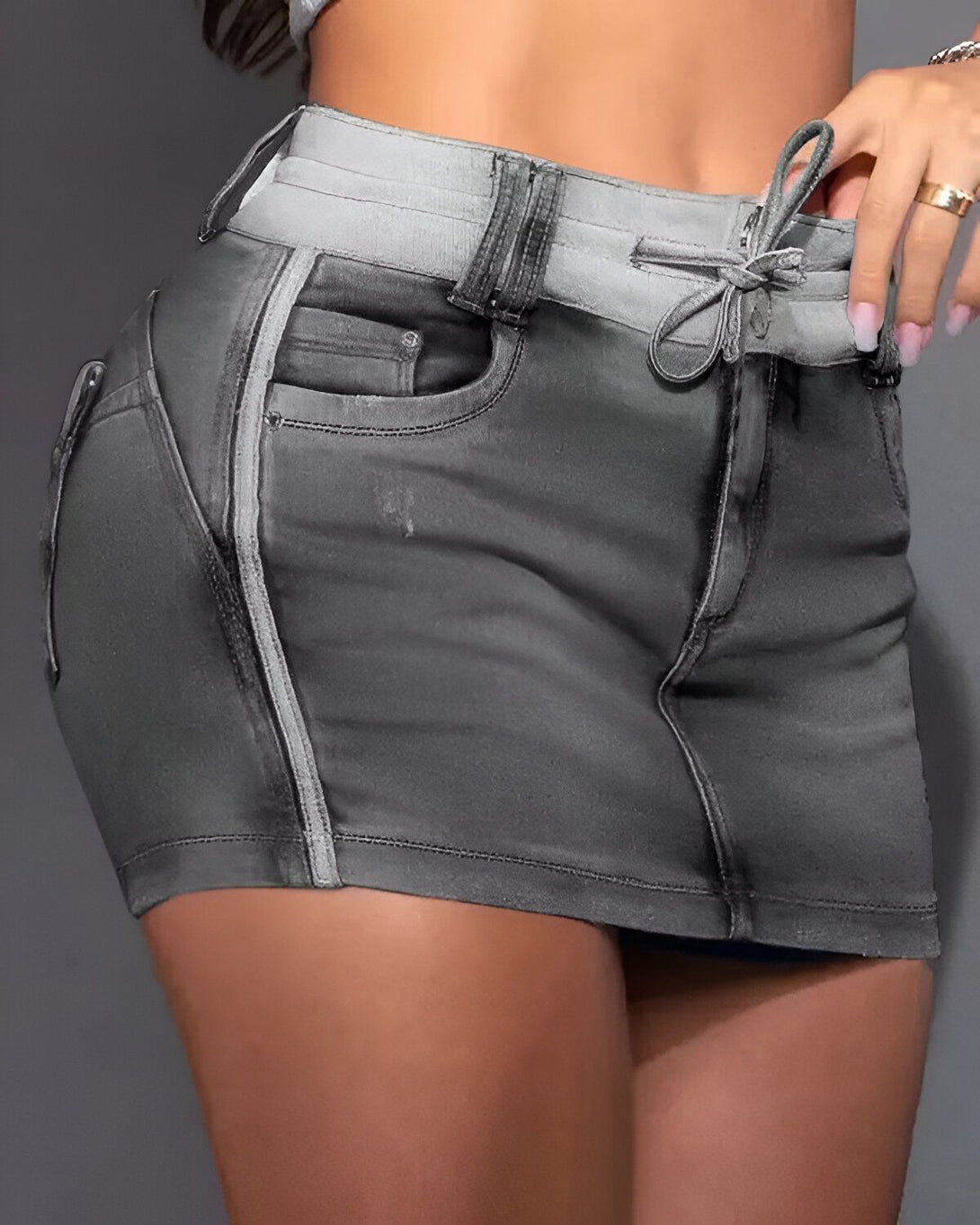 Une image d'une femme portant un short en jean gris avec des détails blancs. Le short est taille haute et a une coupe ajustée. La femme est vue de dos et porte une main sur la hanche.
