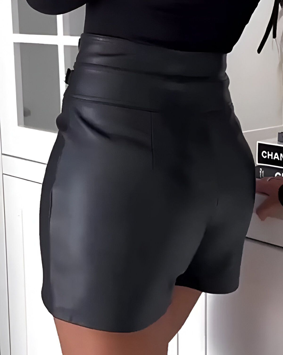 Une femme porte un short en cuir noir taille haute. Le short est ajusté et met en valeur ses courbes.