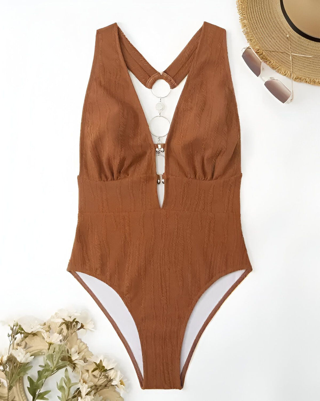 Un maillot de bain une pièce marron avec un anneau argenté sur le devant. Il est échancré sur les côtés et a une doublure blanche.