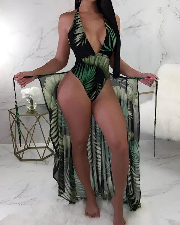 Une femme portant un maillot de bain une pièce noir et vert à motifs de feuilles de palmier. Elle porte également une longue robe de plage transparente à motifs de feuilles de palmier.