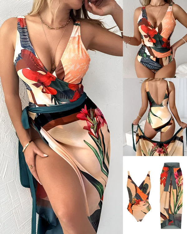Une femme porte un maillot de bain une pièce avec un imprimé floral et un paréo assorti. Le maillot de bain a un décolleté en V profond et des bretelles fines. Le paréo est noué autour de la taille et fendu sur le côté. La femme est debout dans une pose avantageuse et regarde l'appareil photo.