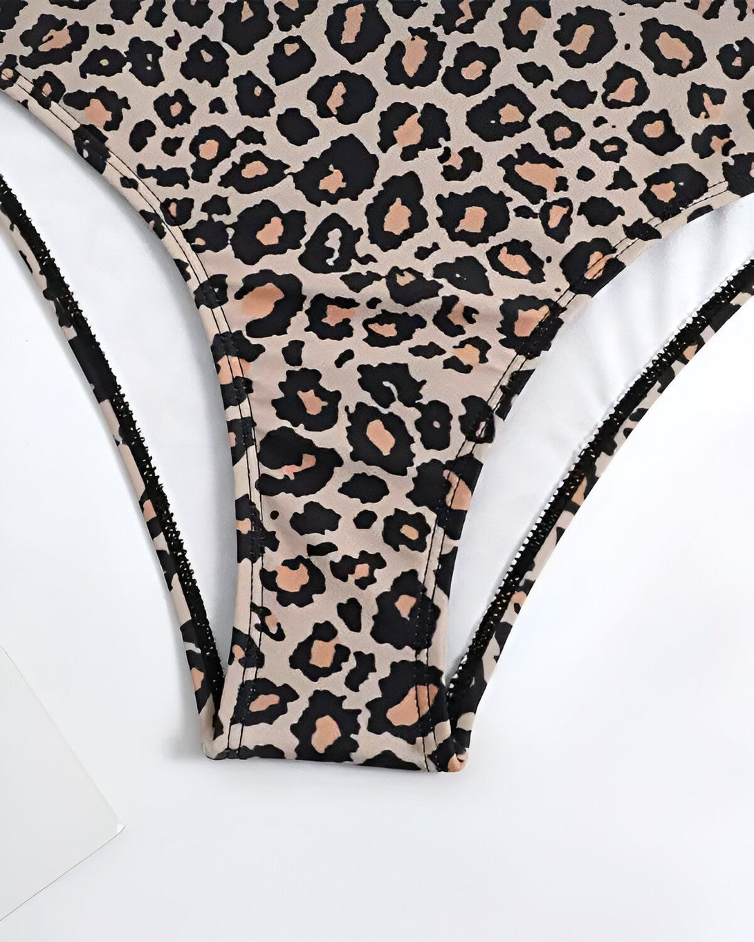 Un maillot de bain une pièce léopard avec un fond beige et des tâches noires.