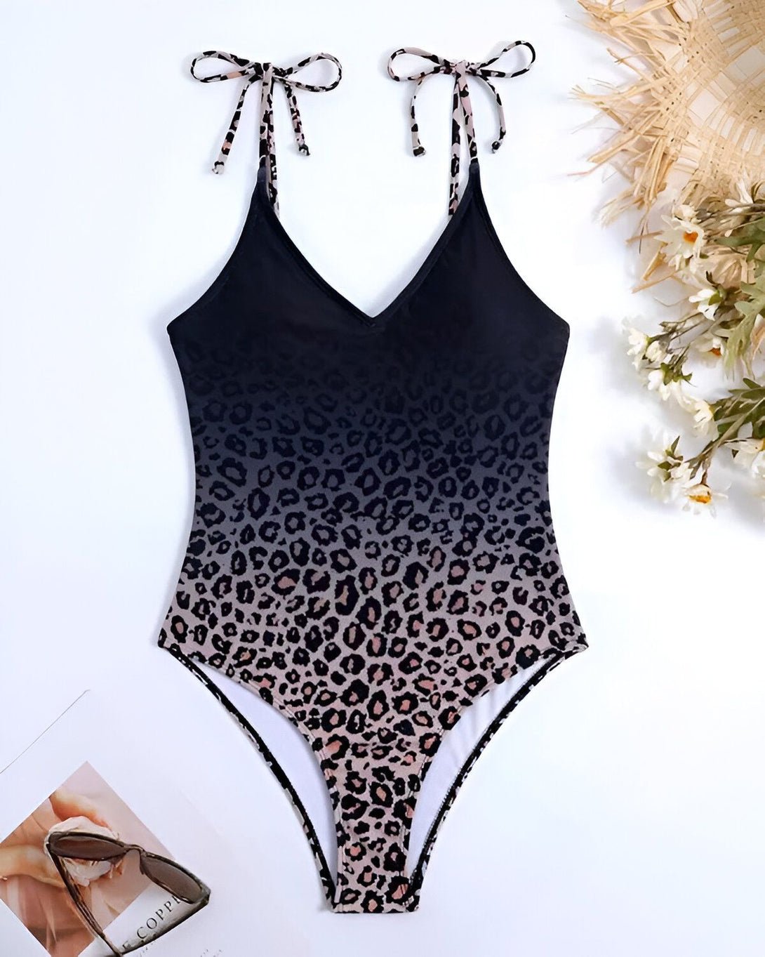L'image représente un maillot de bain une pièce avec un dégradé de couleur noir et marron. Il est de forme triangle avec des bretelles fines et un nœud au niveau de la poitrine. Le maillot de bain est imprimé d'un motif léopard.