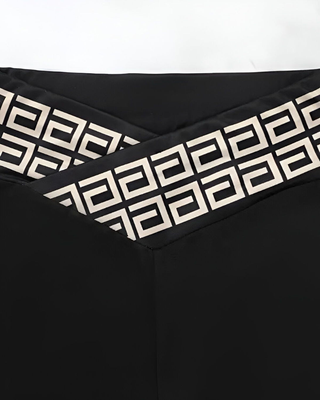 Le haut des leggings noirs est croisé et orné d'un motif géométrique beige et noir.