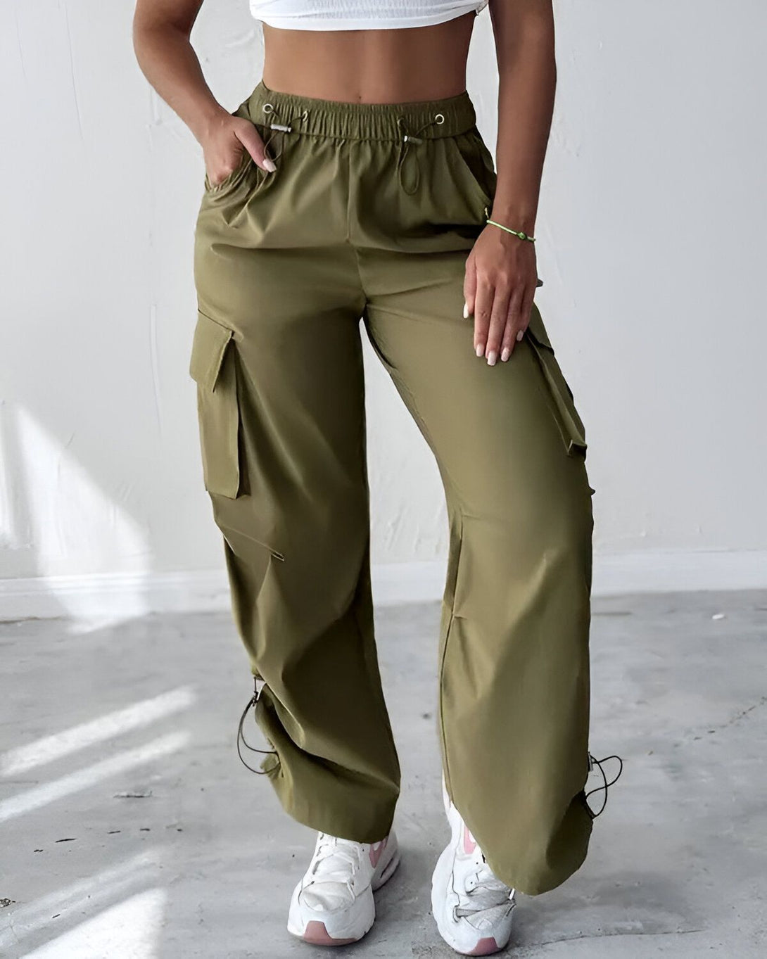 Une femme porte un pantalon cargo vert kaki taille haute avec des poches sur les côtés. Elle porte également un haut blanc et des baskets blanches.