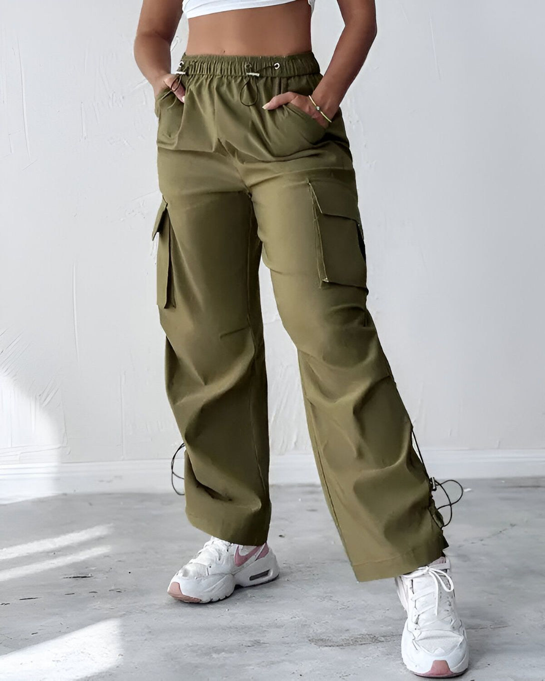 Une femme porte un pantalon cargo vert olive avec des poches sur les côtés. Elle porte également un haut blanc et des baskets blanches.
