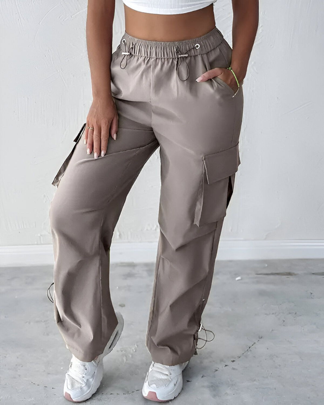 Une femme porte un pantalon cargo beige taille haute avec des poches sur les côtés. Le pantalon est ample et confortable.