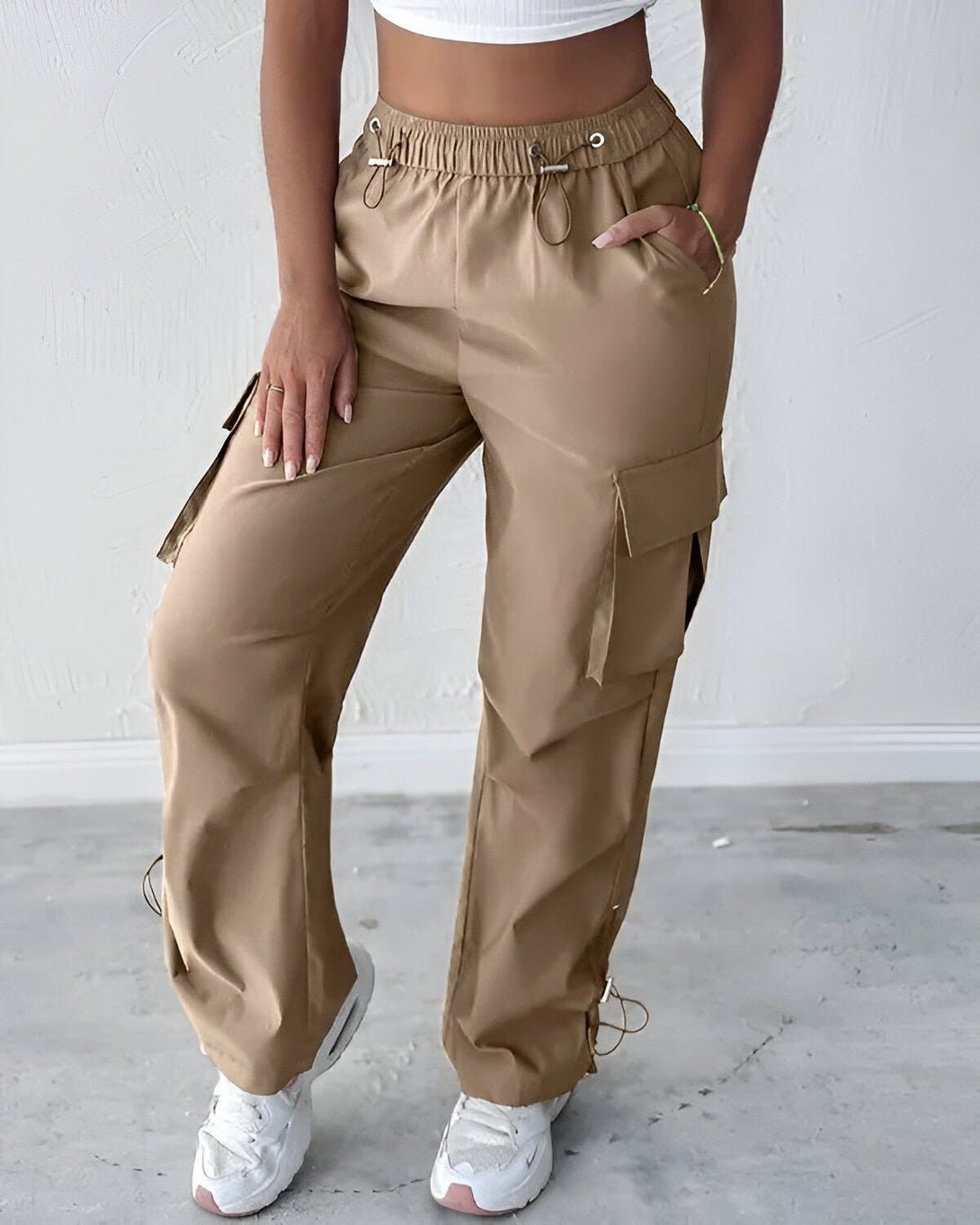 Une femme porte un pantalon cargo beige taille haute avec des poches sur les côtés. Le pantalon est ample et confortable.