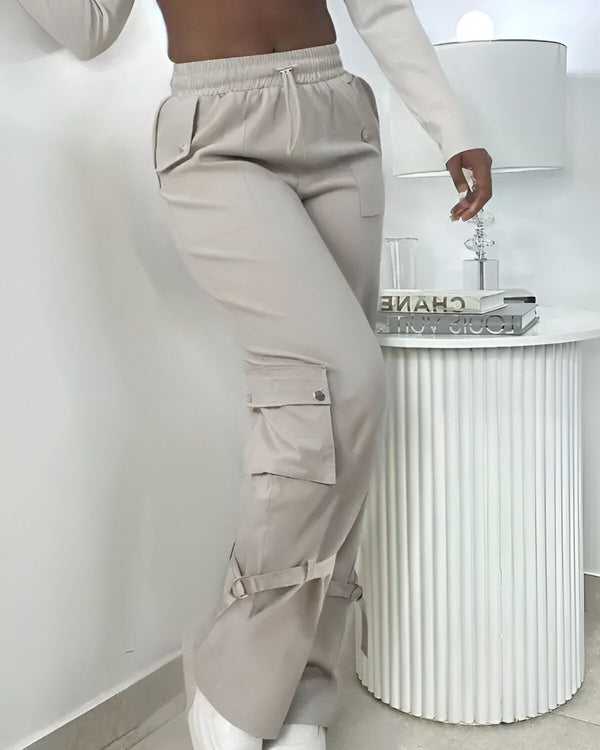 Une femme porte un pantalon cargo beige taille haute avec des poches sur les côtés. Elle porte également un haut blanc et des baskets blanches.