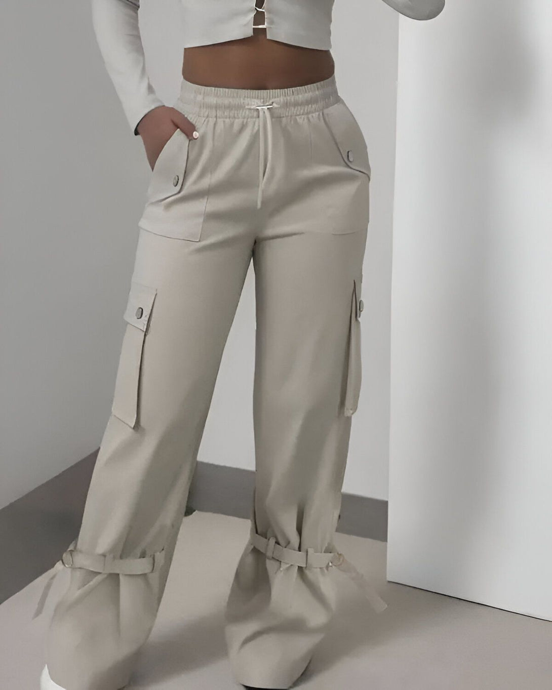 Une femme porte un pantalon cargo beige taille haute avec des poches sur les côtés et des cordons de serrage à la taille. Le pantalon est ample et a une coupe décontractée.