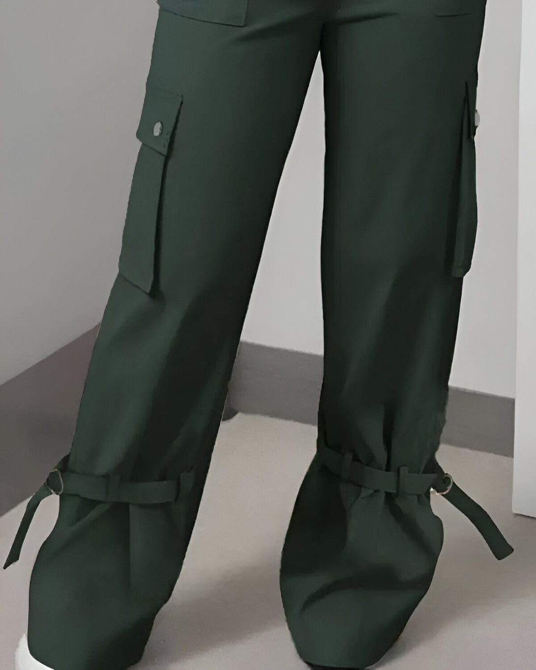 Une image d'un pantalon cargo vert foncé avec des poches et des sangles aux chevilles.