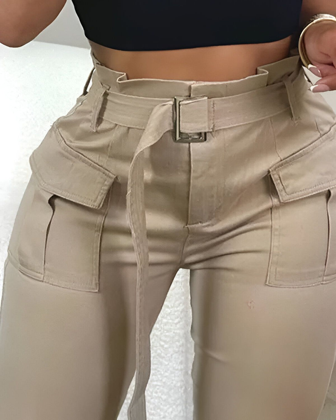 Une femme porte un pantalon cargo beige taille haute avec une ceinture. Le pantalon a des poches sur les côtés et des jambes larges.