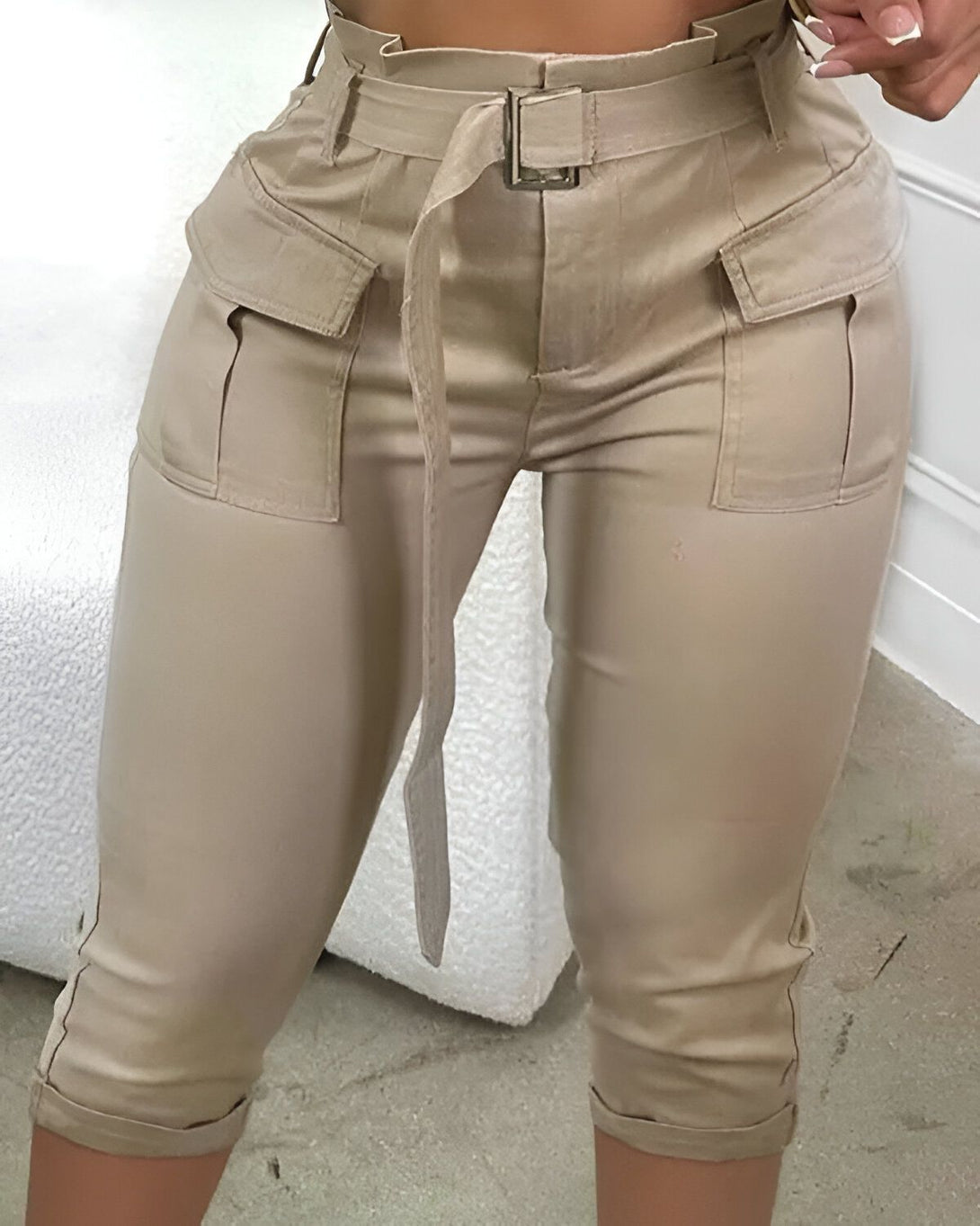Une femme porte un pantalon cargo beige taille haute. Le pantalon est ceinturé et possède des poches cargo sur les côtés.