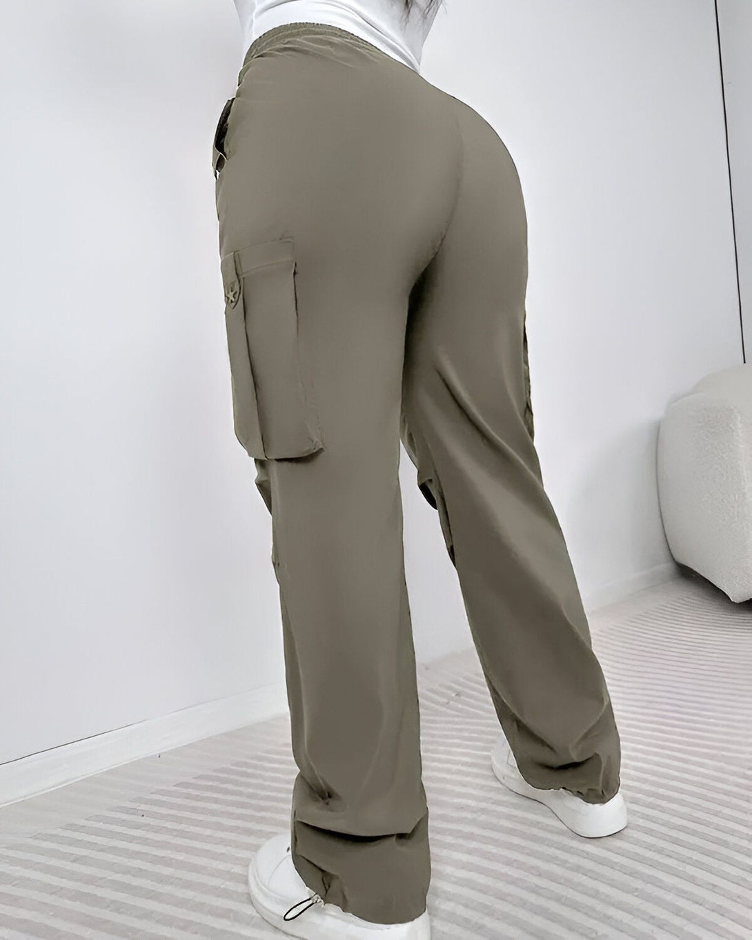Une femme porte un pantalon cargo vert olive taille haute. Le pantalon est ample et a des poches cargo sur les côtés. La femme est vue de dos.