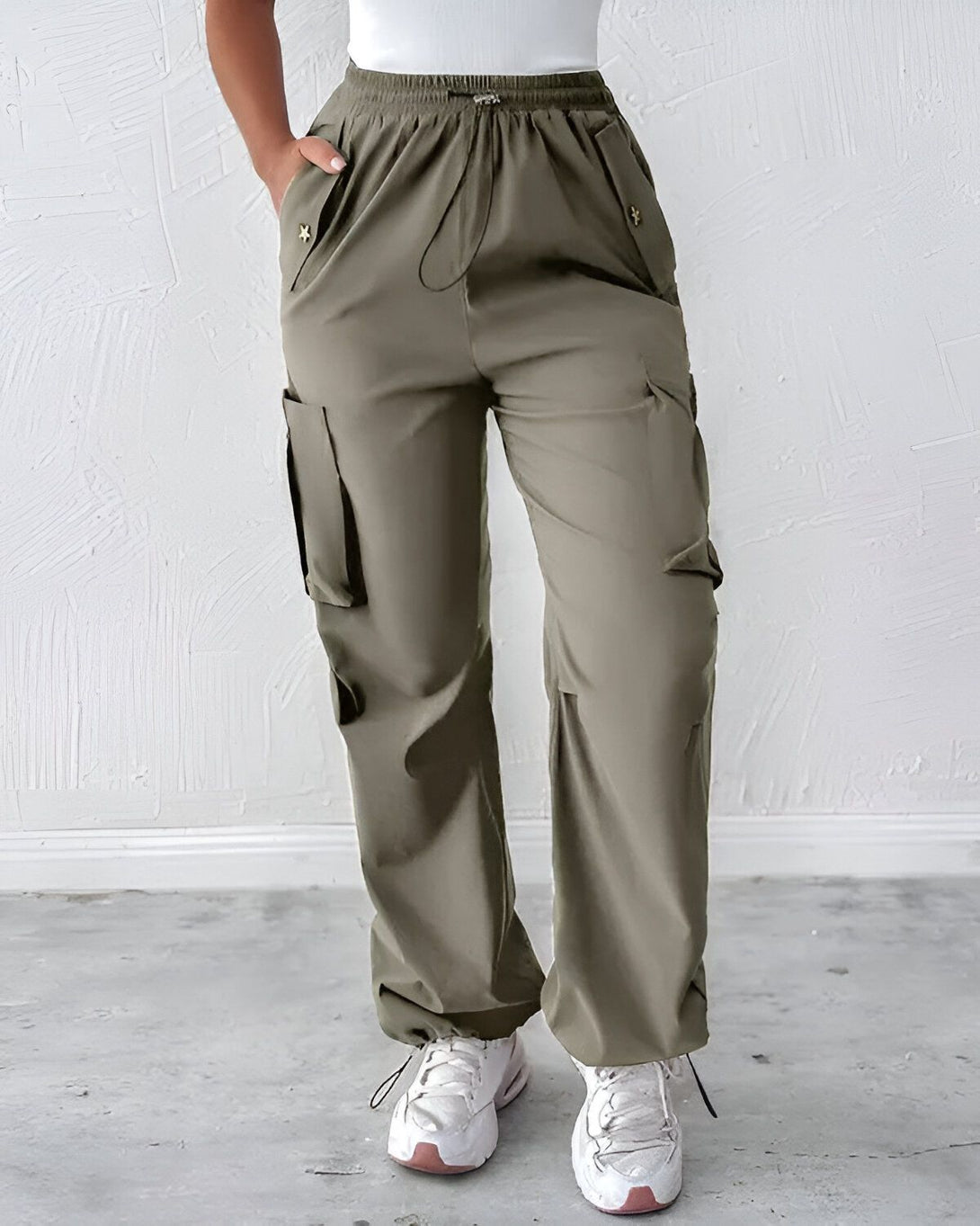 Une femme porte un pantalon cargo vert olive. Le pantalon est ample et a des poches sur les côtés. La femme porte également un haut blanc et des baskets blanches.