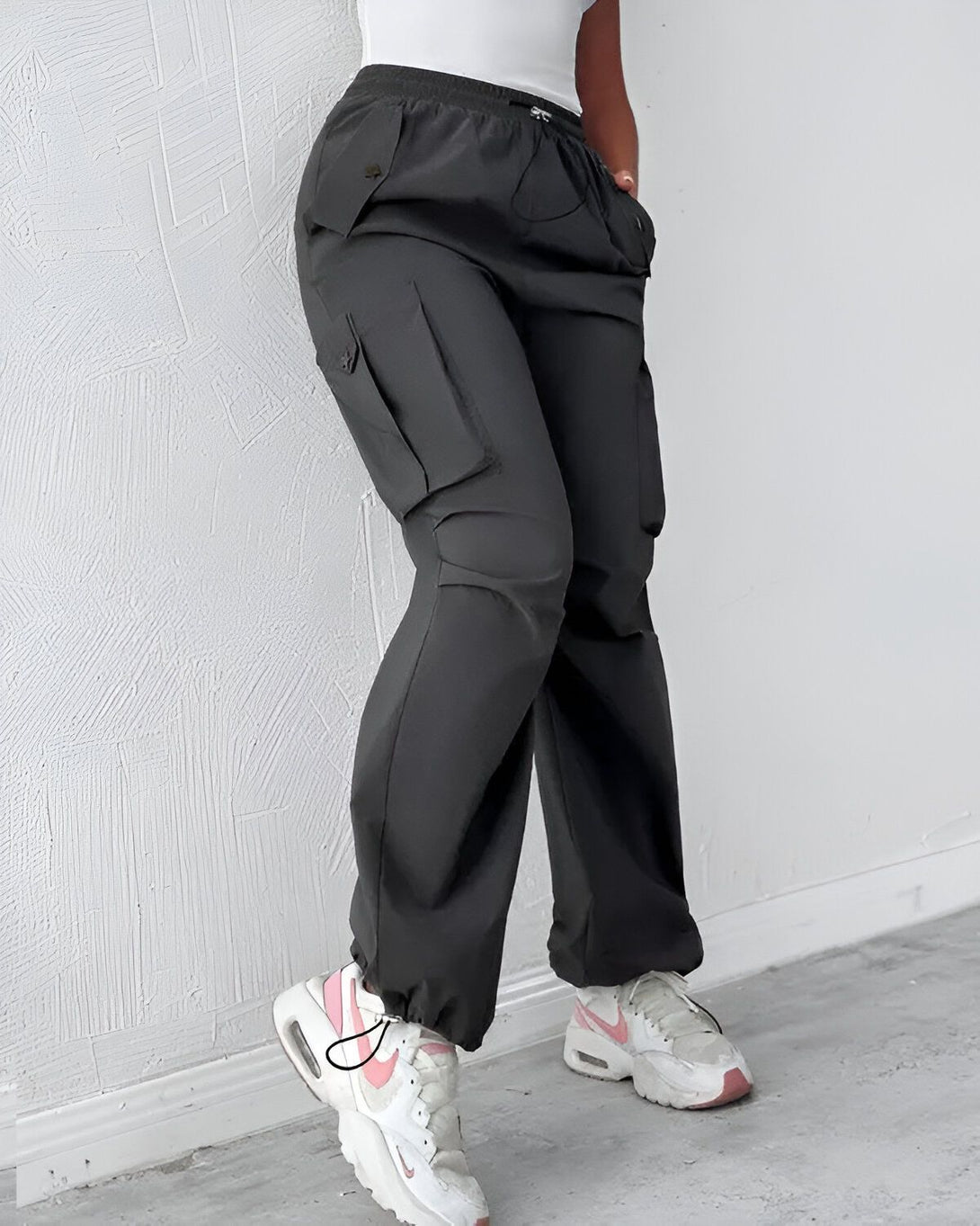 Une femme porte un pantalon cargo noir avec des poches sur les côtés. Elle porte également des baskets Nike Air Max 90 blanches et roses.