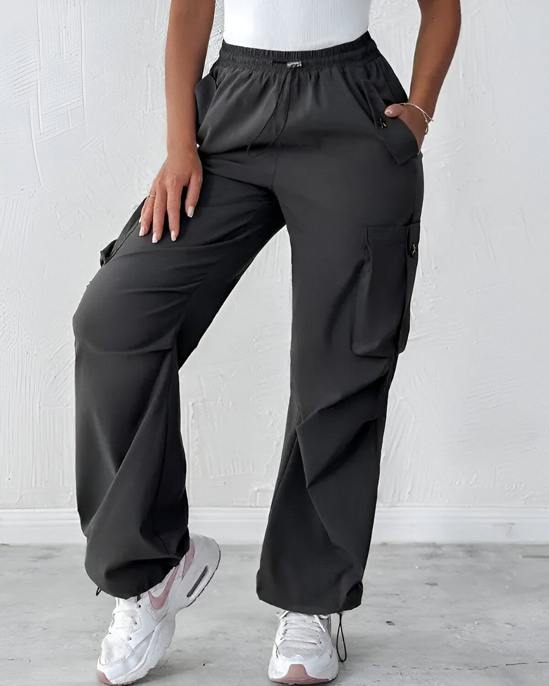 Une femme porte un pantalon cargo noir. Le pantalon est ample et a des poches sur les côtés. La femme porte également un débardeur blanc et des baskets blanches.