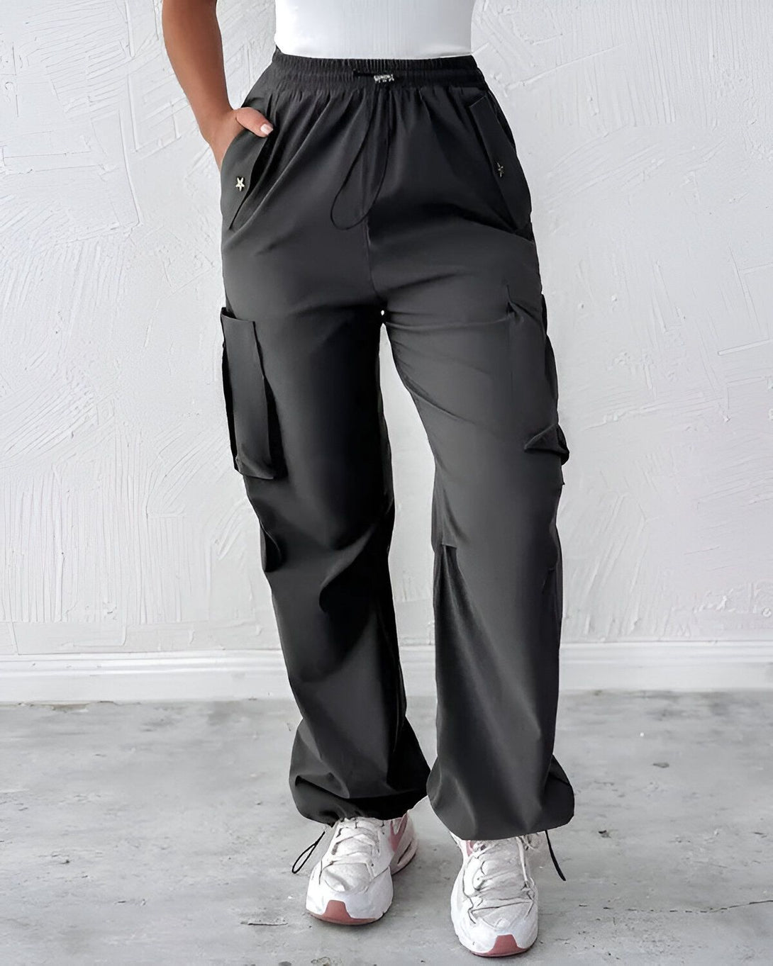 Une femme porte un pantalon cargo noir avec des poches sur les côtés. Elle porte également un haut blanc et des baskets blanches.