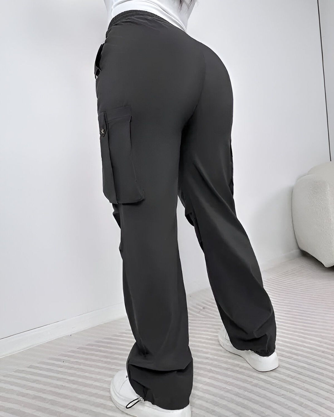 Une femme porte un pantalon cargo noir ample avec des poches sur les côtés. Le pantalon est taille haute et a une coupe droite. La femme est vue de dos et porte des baskets blanches.
