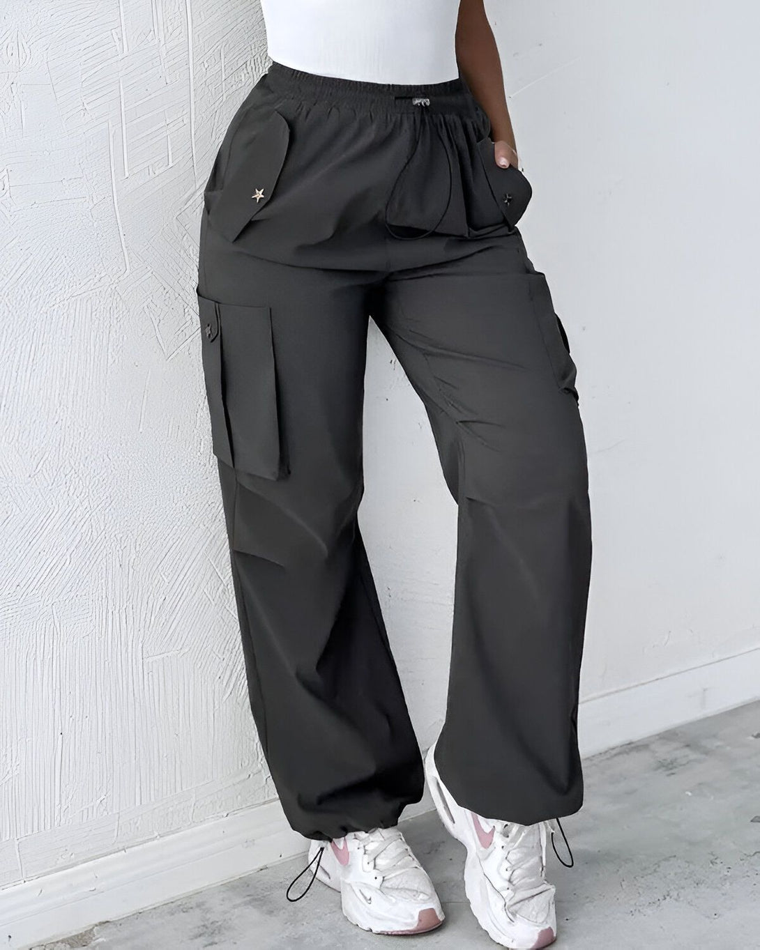 Une femme porte un pantalon cargo noir avec des poches sur les côtés. Elle porte également un haut blanc et des baskets blanches.