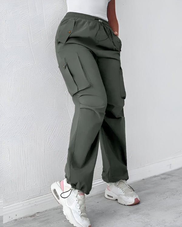 Une femme porte un pantalon cargo vert olive avec des poches sur les côtés. Elle porte également un t-shirt blanc et des baskets blanches et roses.