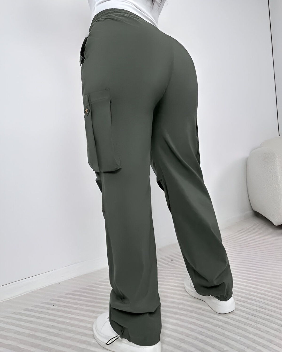 Une femme porte un pantalon cargo vert olive taille haute avec des poches cargo sur les côtés. Le pantalon est ample et a une coupe décontractée.