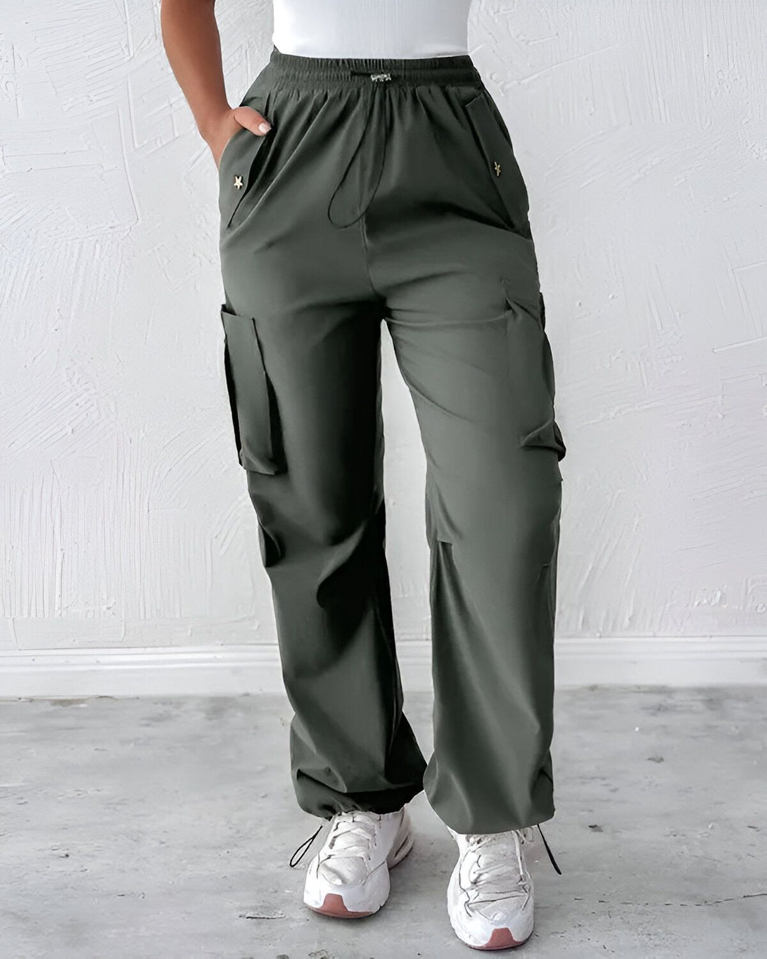 Une femme porte un pantalon cargo vert kaki avec des poches et des étoiles dorées sur les côtés. Elle porte également un haut blanc et des baskets blanches.