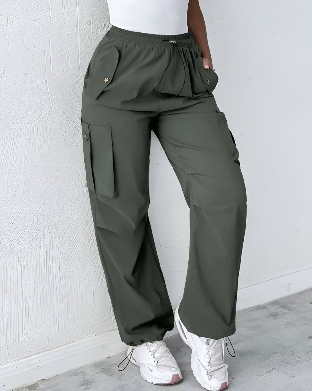 Une femme porte un pantalon cargo vert kaki avec des étoiles dorées sur les poches. Elle porte également un haut blanc et des baskets blanches.