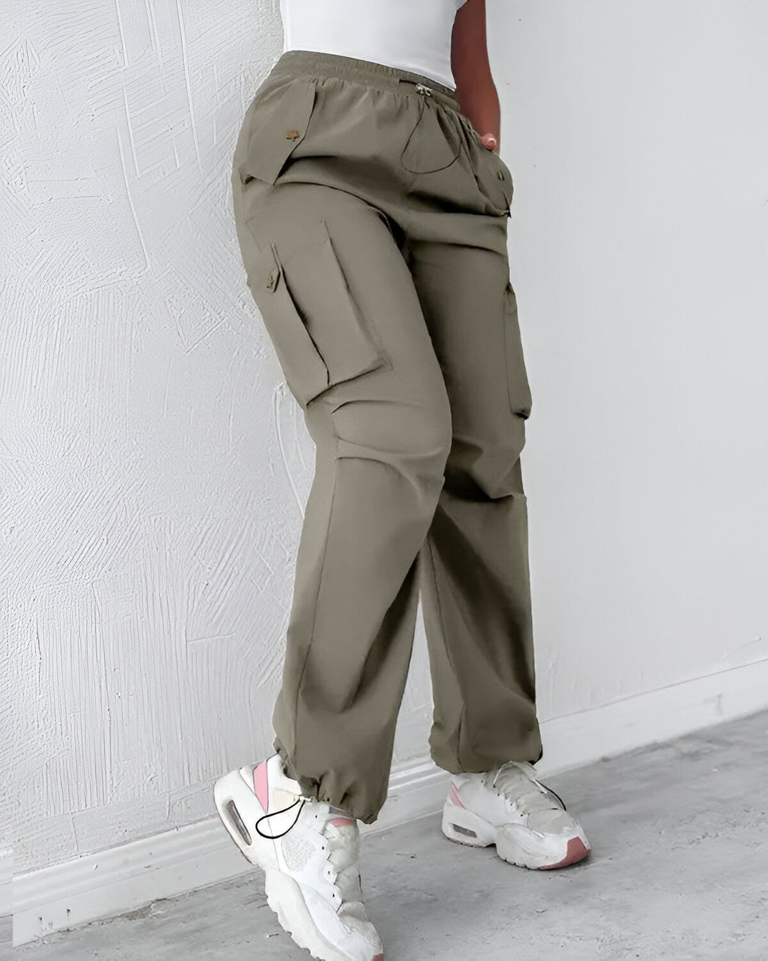 Une femme porte un pantalon cargo vert olive avec des poches sur les côtés. Elle porte également des baskets blanches et un haut blanc.