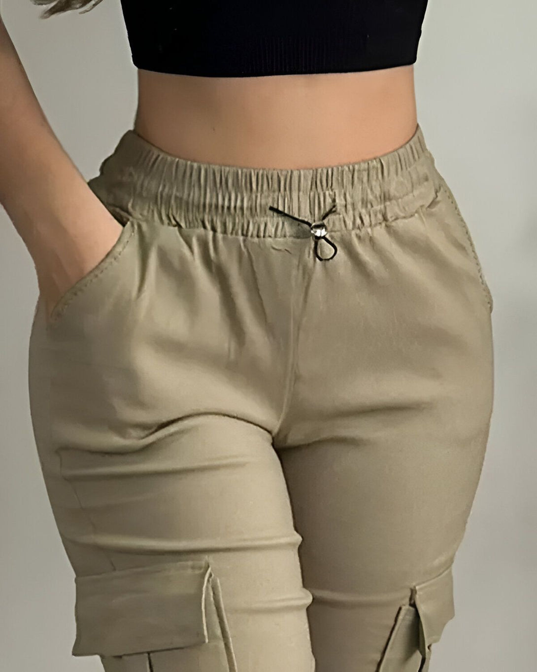Une femme porte un pantalon cargo beige taille haute avec des poches et un cordon de serrage à la taille. Elle porte également un haut noir court.