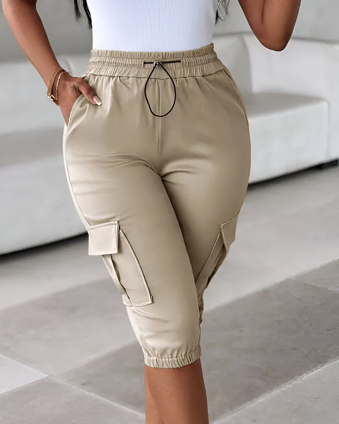 Une femme porte un pantalon cargo beige taille haute. Le pantalon est ample et a des poches cargo sur les côtés. La femme est debout, la main dans la poche.