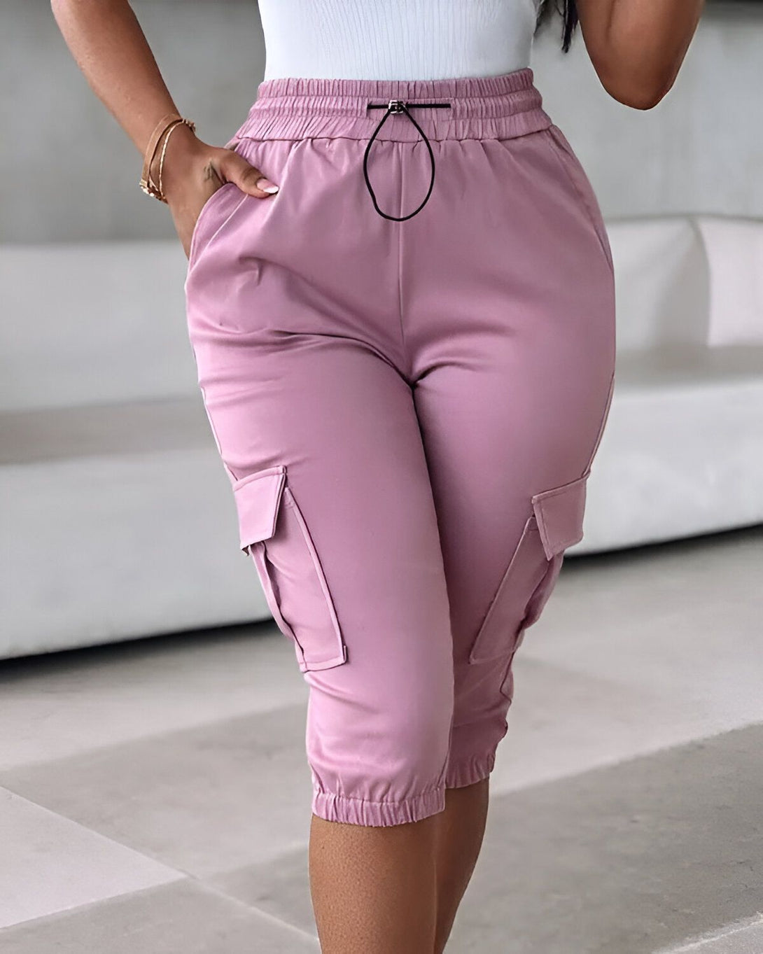 Une femme porte un pantalon cargo rose. Le pantalon est taille haute et possède des poches cargo sur les côtés. La femme est vue de face et porte un haut blanc.