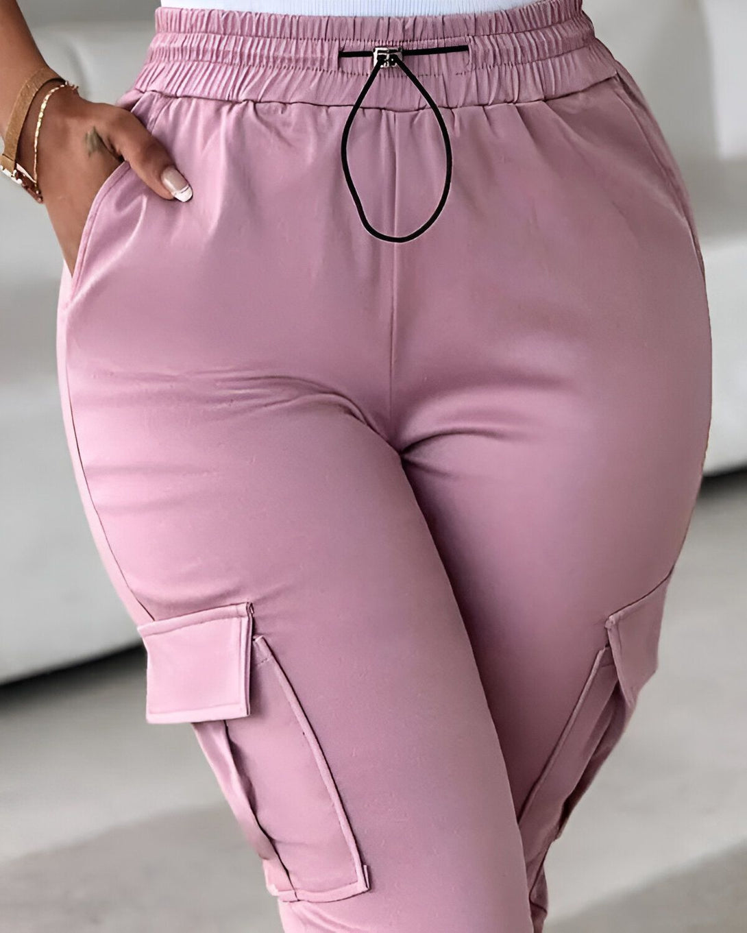 Une femme porte un pantalon cargo rose. Le pantalon est taille haute et possède une coupe ample. Il est doté de deux poches cargo sur les côtés et d'un cordon de serrage à la taille. La femme porte également un haut blanc et des baskets blanches.