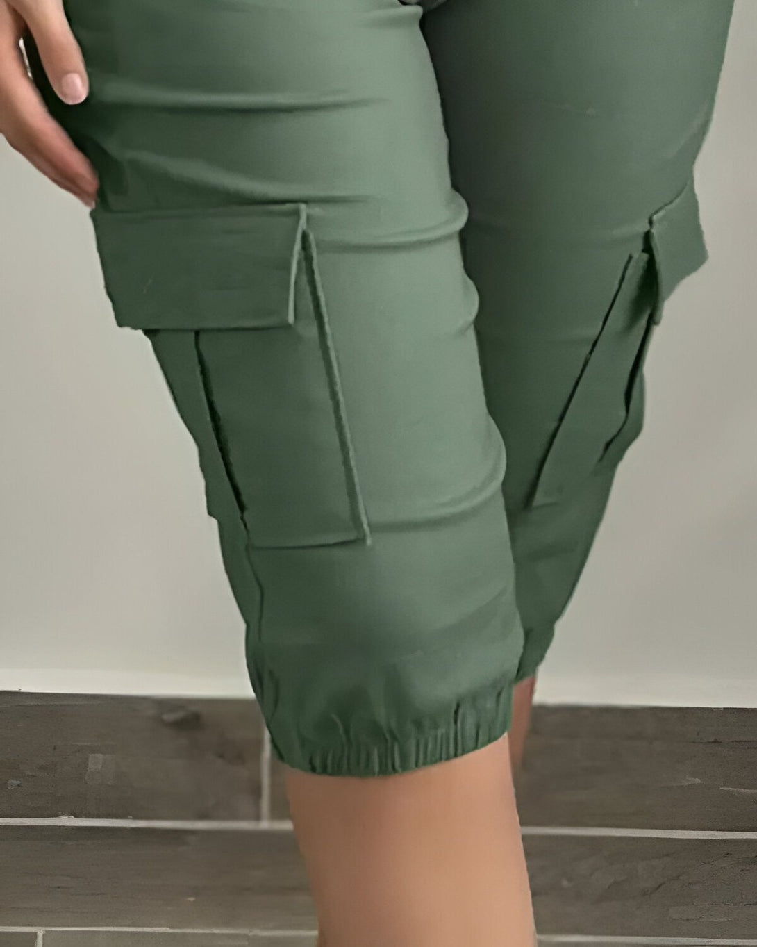 Une femme porte un pantalon cargo vert olive. Le pantalon est ample et a des poches sur les côtés. La femme est vue de côté et porte des talons hauts noirs.