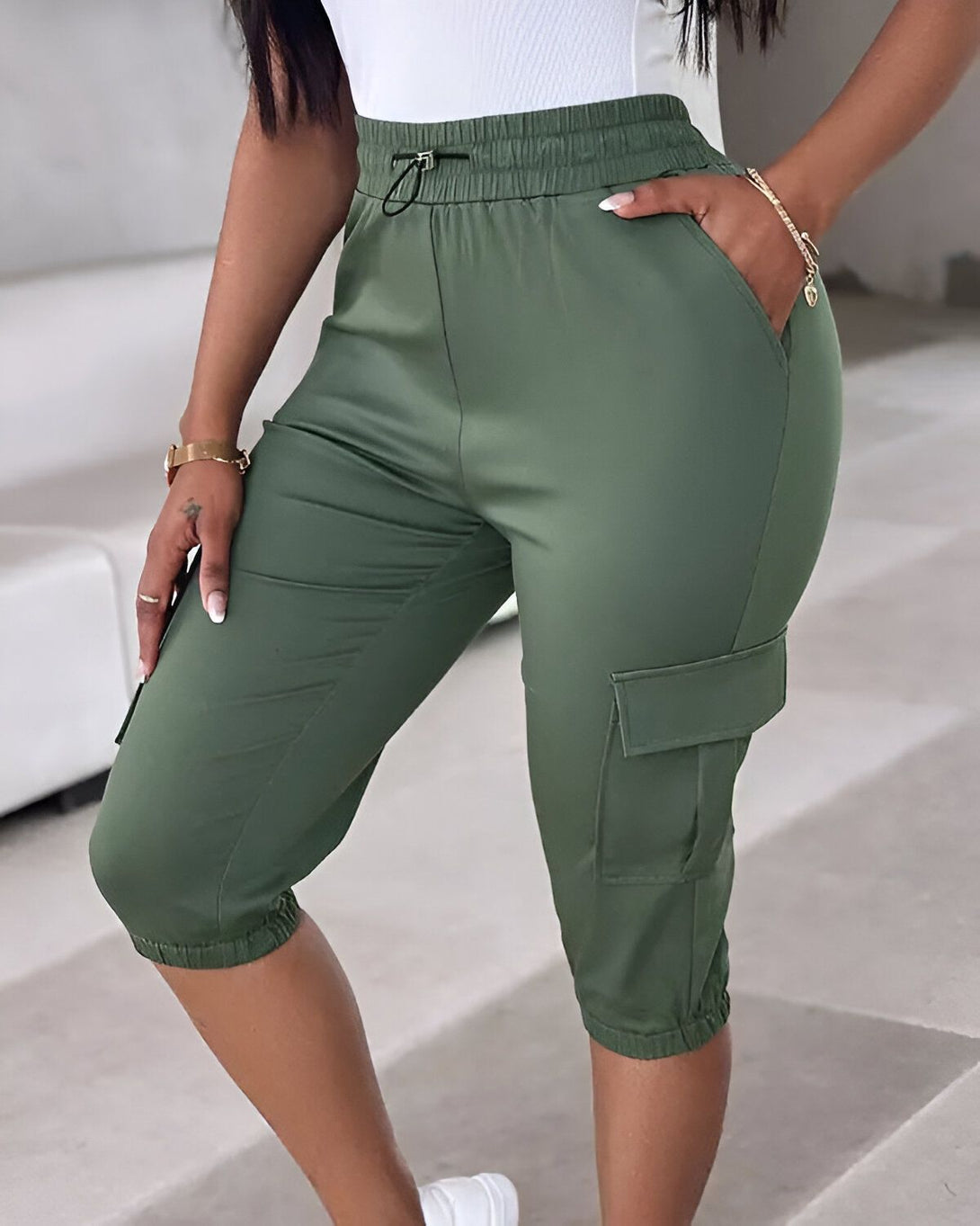 Une femme porte un pantalon cargo vert olive taille haute. Le pantalon est ample et a des poches cargo sur les côtés. La femme est vue de dos et porte un haut blanc.