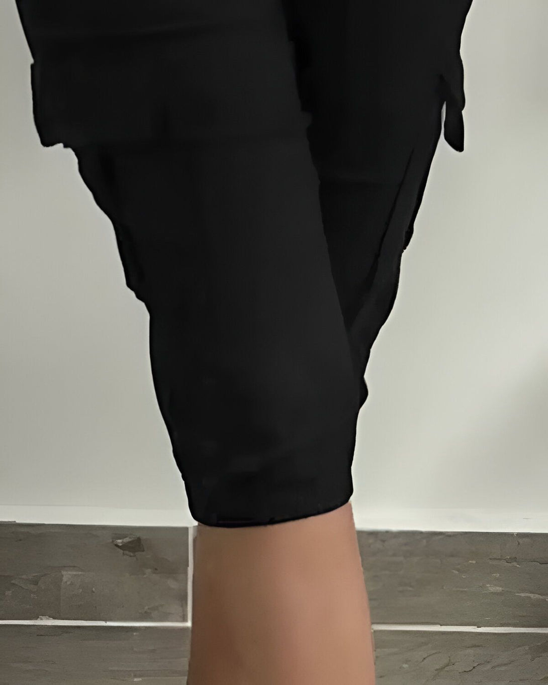 Une personne portant un pantalon cargo noir est debout sur un sol carrelé. Le pantalon est ample et a des poches sur les côtés. La personne est vue de face et ses pieds sont légèrement écartés.