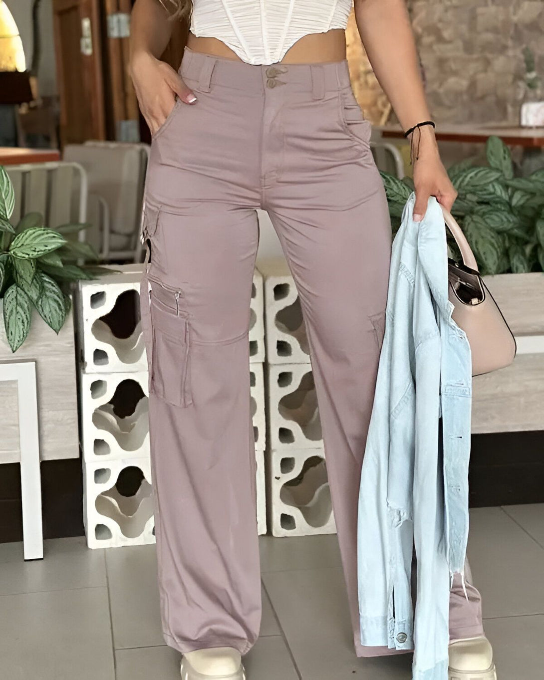Une femme porte un pantalon cargo rose et un corset blanc. Elle a une veste en jean bleu clair à la main.