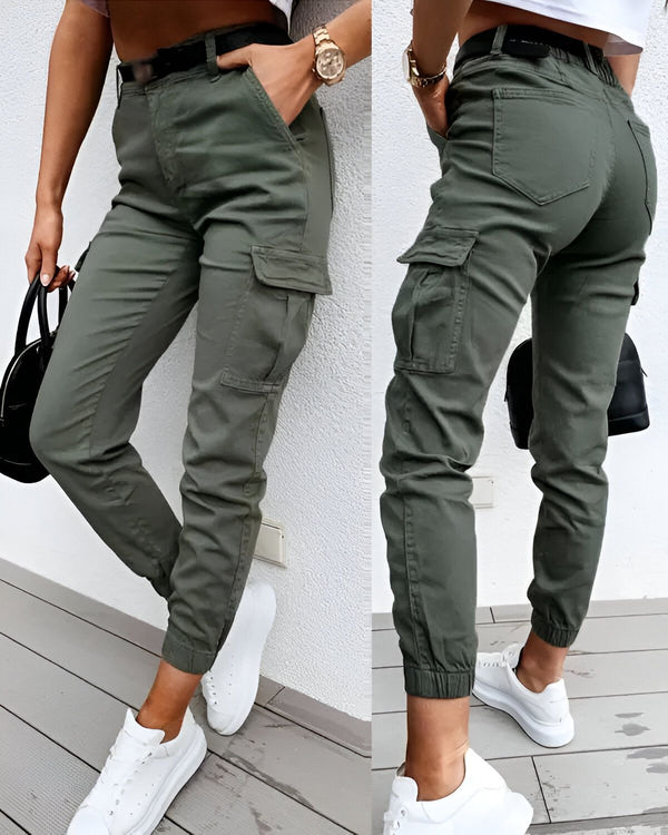 Une image d'une femme portant un pantalon cargo vert olive. Le pantalon est taille haute et possède plusieurs poches. La femme porte également un haut blanc et des baskets blanches.