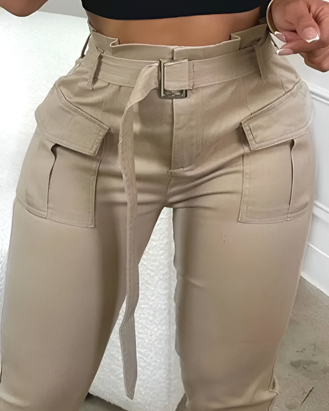 Une femme porte un pantalon cargo beige taille haute avec une ceinture. Le pantalon a des poches sur les côtés et des fermetures éclair aux chevilles.