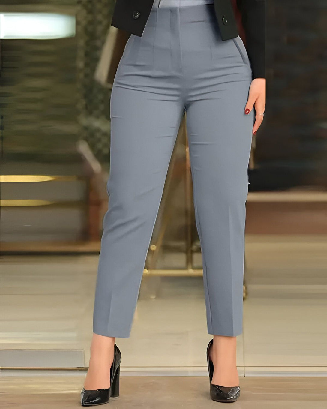 Une femme porte un pantalon bleu marine taille haute et des escarpins noirs. Elle porte également une veste noire.