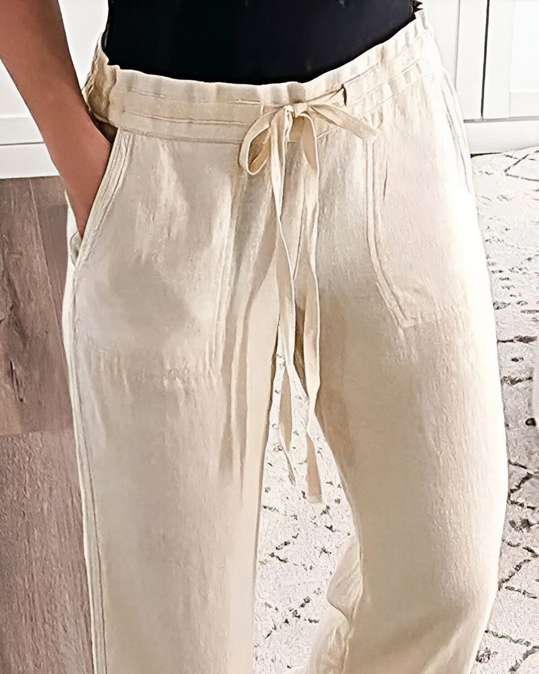 Une femme porte un pantalon beige taille haute avec un cordon de serrage à la taille. Le pantalon est ample et a des poches sur les côtés.