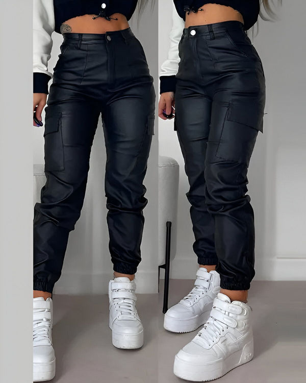 Une image d'une femme portant un pantalon cargo en similicuir noir. Le pantalon est taille haute et possède des poches cargo sur les côtés. La femme porte également un haut court noir et des baskets blanches.