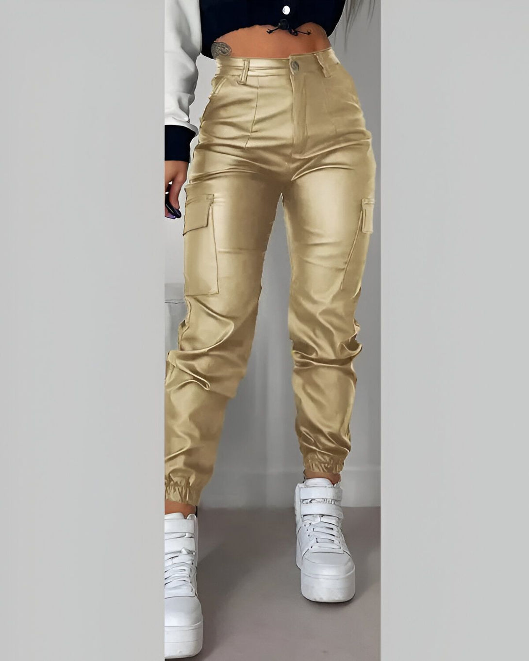 Une image d'un mannequin portant un pantalon cargo taille haute en similicuir doré. Le pantalon est ample et possède des poches cargo sur les côtés. Le mannequin porte également un haut court blanc et des baskets blanches.