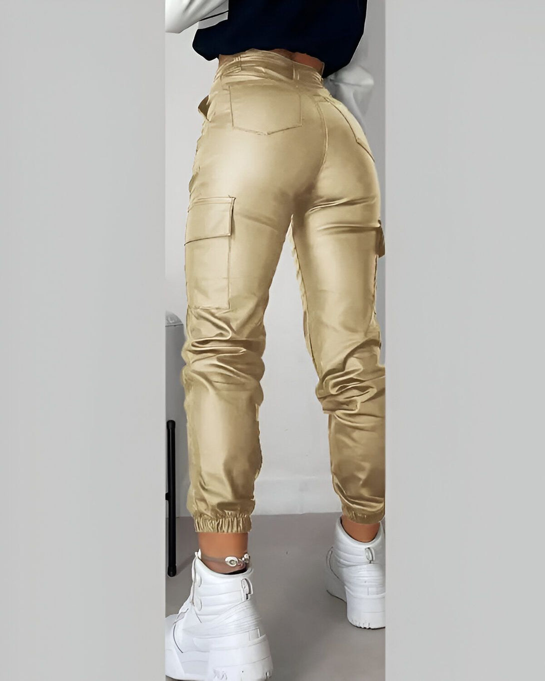 Une femme porte un pantalon cargo doré taille haute. Le pantalon est ample et a des poches cargo sur les côtés. La femme est vue de dos et porte des baskets blanches.