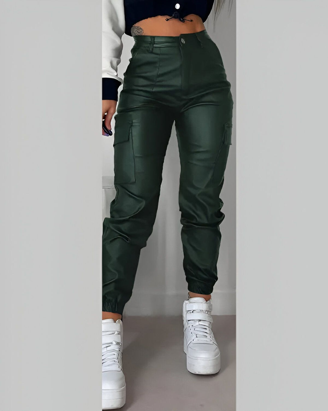 Une femme porte un pantalon cargo vert foncé en similicuir avec des poches sur les côtés. Elle porte également un haut court blanc et des baskets blanches.