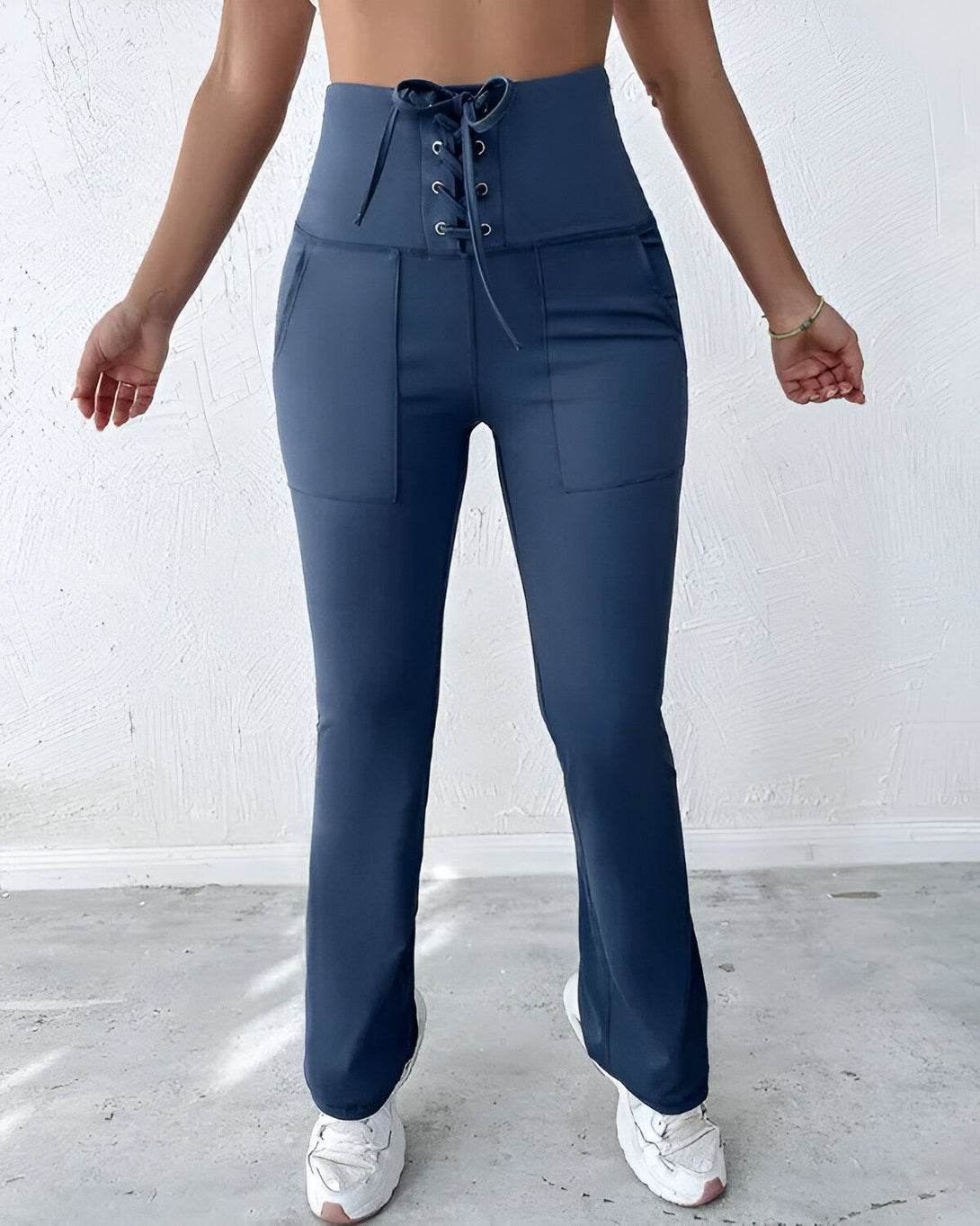 Une femme porte un pantalon de yoga bleu marine taille haute avec un laçage à la taille. Le pantalon est évasé et possède des poches.